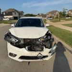 White Nissan sedan with a smashed front end, junk car removal