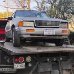 Silver Chrysler sedan loaded on a flatbed tow truck, towing service