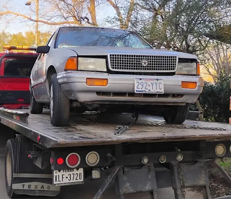 Silver Chrysler sedan loaded on a flatbed tow truck, towing service
