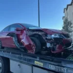 Wrecked red sedan on a Century flatbed tow truck, scrap car buying