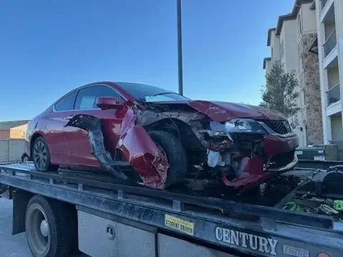 Wrecked red sedan on a Century flatbed tow truck, scrap car buying