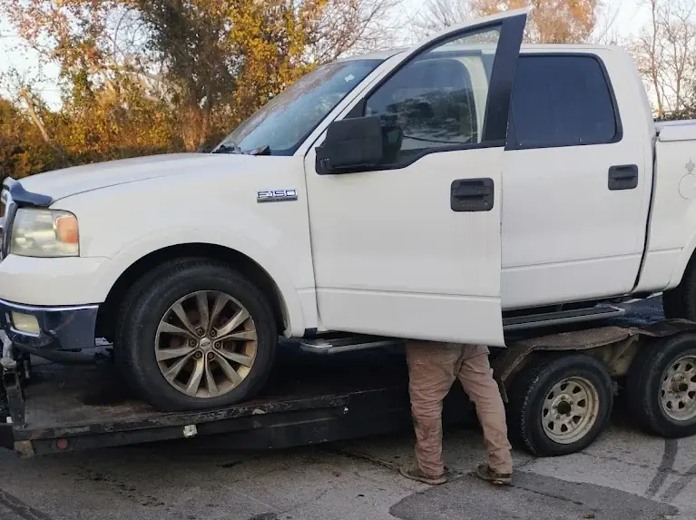 White Ford F-150 pickup loaded on a trailer for free junk car towing